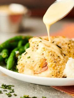 someone is pouring sauce on some food in a white plate with green beans and mashed potatoes