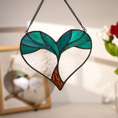 a heart shaped stained glass window hanging from a chain with flowers in vases behind it