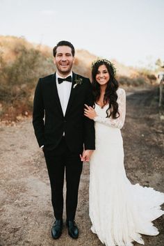 a man and woman standing next to each other in front of a dirt road with trees