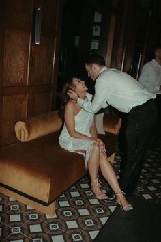 a man kneeling down next to a woman on a couch in a room with tile flooring