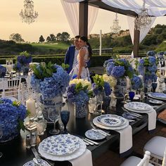 a couple standing next to each other at a table with blue and white plates on it