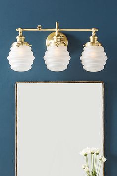 a bathroom vanity with three lights and a mirror on the wall next to flowers in a vase