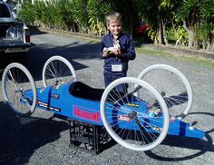 a young boy standing next to an old fashioned car with wheels on it's rims