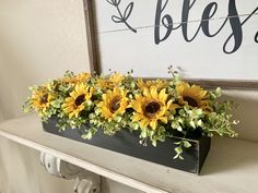 sunflowers are in a wooden box on a mantle with a sign above it