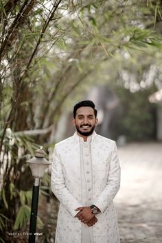 a man standing in front of a tree with his hands on his hips and wearing a white suit