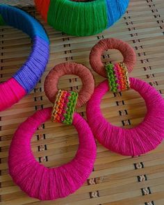 three different colored yarns are sitting on a bamboo mat next to two colorful hoop earrings