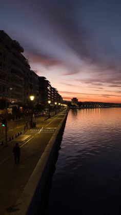 a person walking along the edge of a body of water at night with buildings in the background