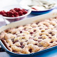 a berry cobbler in a blue baking dish on a table with raspberries