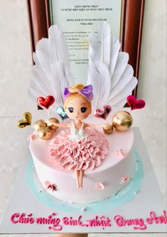 a birthday cake with a doll on top and decorations around the edges, sitting in front of a framed photo