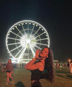 a woman standing in front of a ferris wheel at night with her hand up to her face