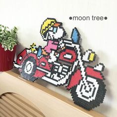 an image of a motorcycle made out of perler beads on a shelf next to a potted plant