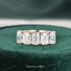 an emerald cut diamond ring sits on top of a green velvet box