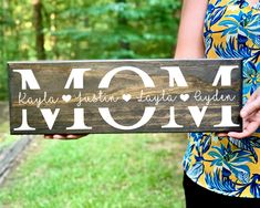 a woman holding up a wooden sign that says mom