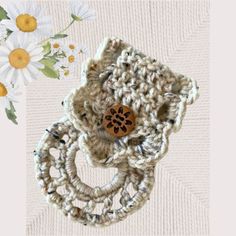 a crocheted object with a wooden button on it's center piece and daisies in the background