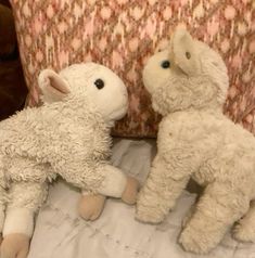 two stuffed animals sitting on top of a bed next to each other, one white and the other light brown