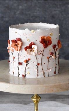 a white cake with red and orange flowers painted on it's side, sitting on a gold pedestal