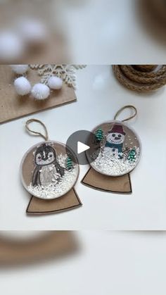 two snowman ornament hanging from strings on a white table with other decorations