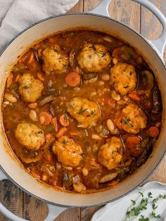 a pot filled with meat and vegetable stew on top of a wooden table next to spoons