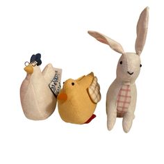 three stuffed animals sitting next to each other on a white surface with one holding an egg