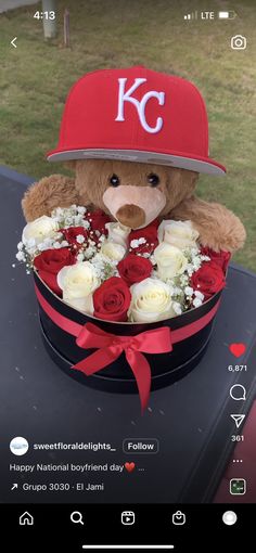 a teddy bear wearing a baseball cap and holding roses in a black box with red ribbon