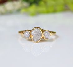 three stone ring sitting on top of a white surface with flowers in the back ground