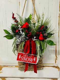 a basket filled with red flowers and greenery next to a sign that says let it snow