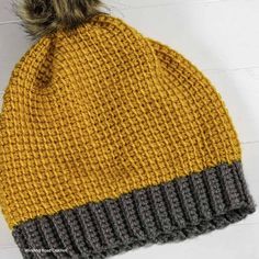 a yellow and grey knitted hat with a pom - pom on top