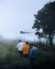 three men standing in tall grass near a fence on a foggy, overcast day