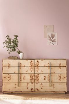 a wooden dresser sitting in front of a pink wall with a potted plant on top