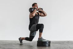 a man in black shirt and grey pants squatting on a round object with one leg up