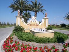 a sign that is in front of some flowers and trees with palm trees behind it