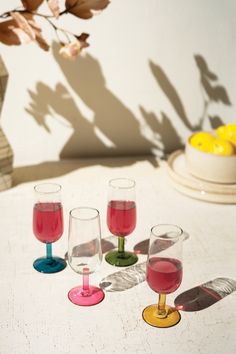 four wine glasses sitting on top of a table next to a vase with lemons