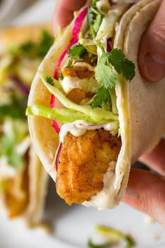 a person holding up a taco filled with meat and veggies on it