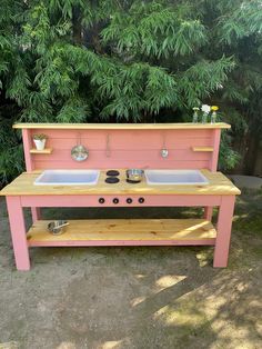 a pink outdoor kitchen with two sinks and pot holders on the top shelf, in front of some trees