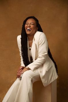 a woman with dreadlocks sitting on a wall smiling and wearing a white suit