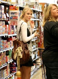 two women shopping in a grocery store with one looking at her cell phone while the other looks on