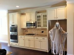 a kitchen decorated for halloween with white cabinets and ghost mask hanging from the wall above the stove