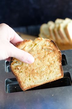 a person is holding up a piece of bread on a toaster tray with slices of bread in the background