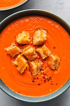 two bowls of tomato soup with croutons on top