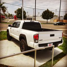 a white truck parked on the side of a road next to a parking lot with palm trees in the background