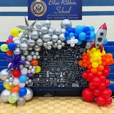 balloons are arranged in the shape of a rocket ship and stars on a chalkboard