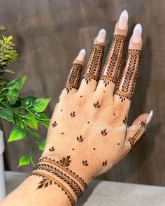 a woman's hand with henna tattoos on it, next to a potted plant