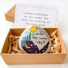 a painted rock in a wooden box with a poem on it that reads, under the same sky