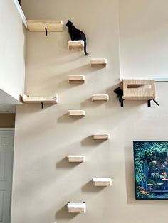 a cat sitting on top of wooden shelves in a living room next to a painting