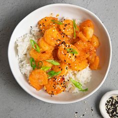 a white bowl filled with rice and shrimp on top of a gray surface next to a spoon