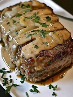 a piece of meat covered in gravy on a white plate with green garnish