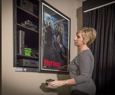 a woman standing in front of a movie poster holding a remote control and looking at it