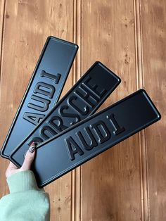 two black metal signs with the words audi and porsche on them, one being held up by a woman's hand