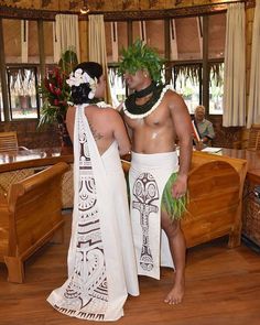 two people dressed in native clothing standing next to each other on a wooden floored room