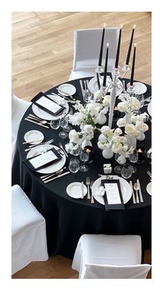 a black table cloth with white flowers and candles is set for an elegant dinner party